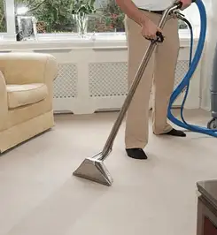 Professional carpet cleaner using a hot-water extraction wand and hose machine in a living room in Akron, OH.