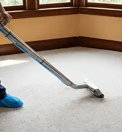 Steam carpet cleaning technician using a hot-water extraction wand on a residential carpet, wearing blue protective shoe covers Akron, OH.
