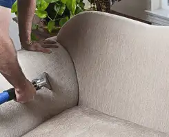 Professional upholstery cleaner deep-cleaning a fabric sofa with a handheld extraction tool and hose in Akron, OH.